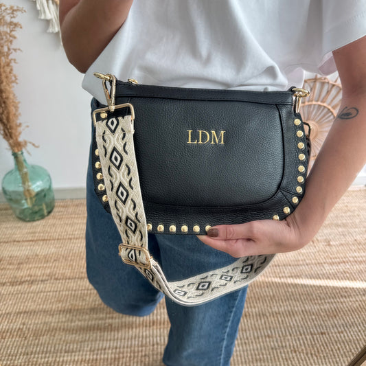 Bandolera ovalada piel tachuelas negro iniciales bordadas