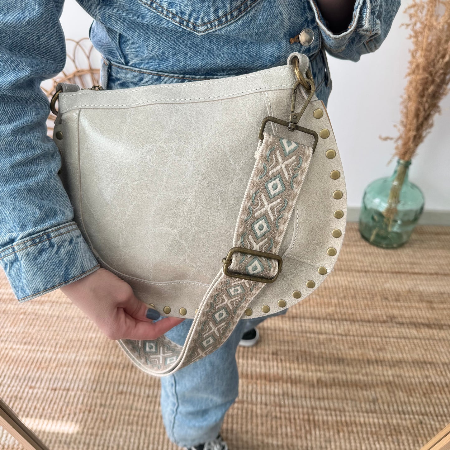 Bandolera ovalada piel tachuelas beige iniciales bordadas herrajes cobre
