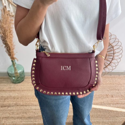 Bandolera ovalada piel tachuelas granate iniciales bordadas