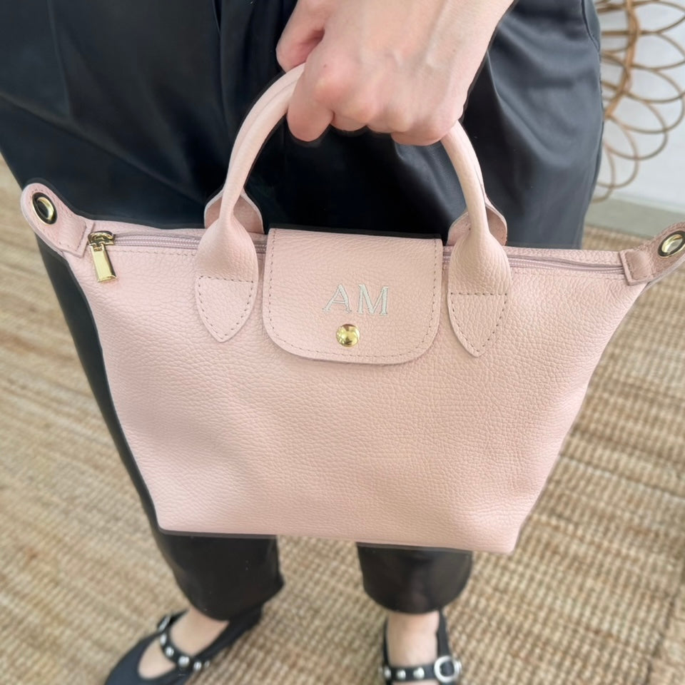 Bolso ovalado piel rosa solapa iniciales bordadas