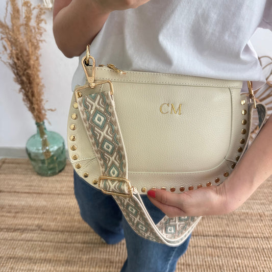 Bandolera ovalada piel tachuelas beige iniciales bordadas