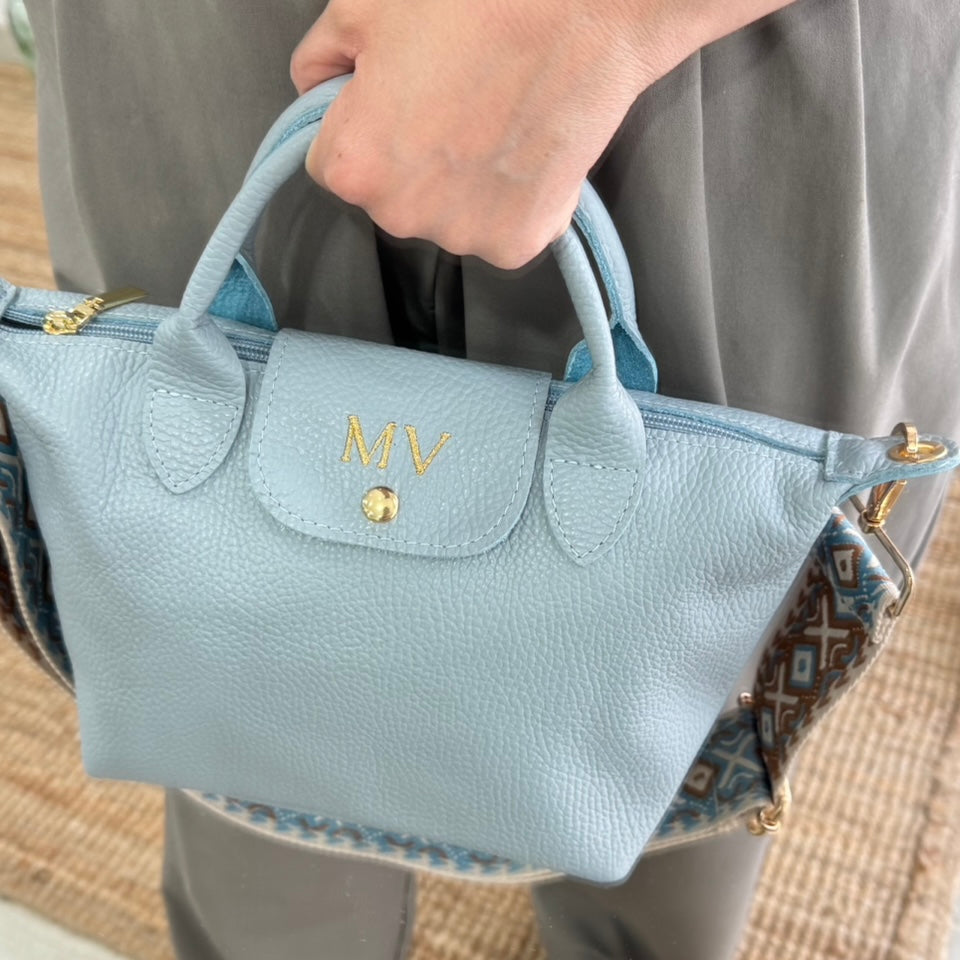 Bolso ovalado piel celeste solapa iniciales bordadas
