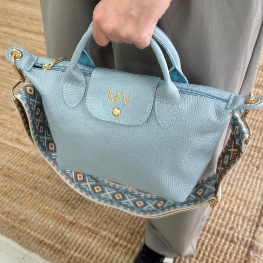 Bolso ovalado piel celeste solapa iniciales bordadas