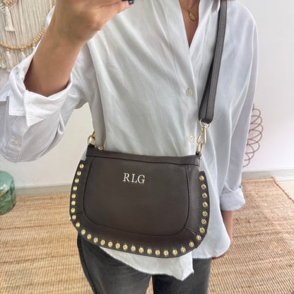 Bandolera ovalada piel tachuelas marrón iniciales bordadas