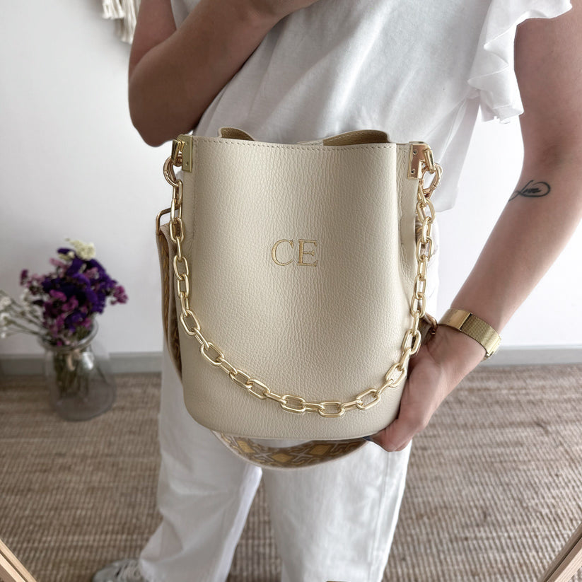 Bolso bucket piel beige cadena dorada iniciales bordadas