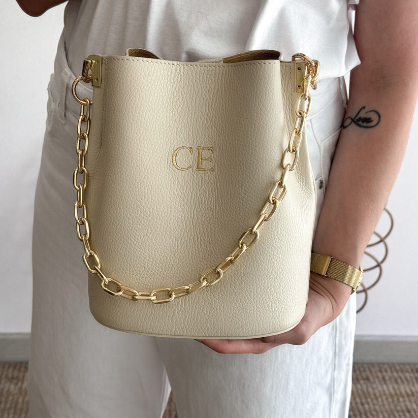 Bolso bucket piel beige cadena dorada iniciales bordadas